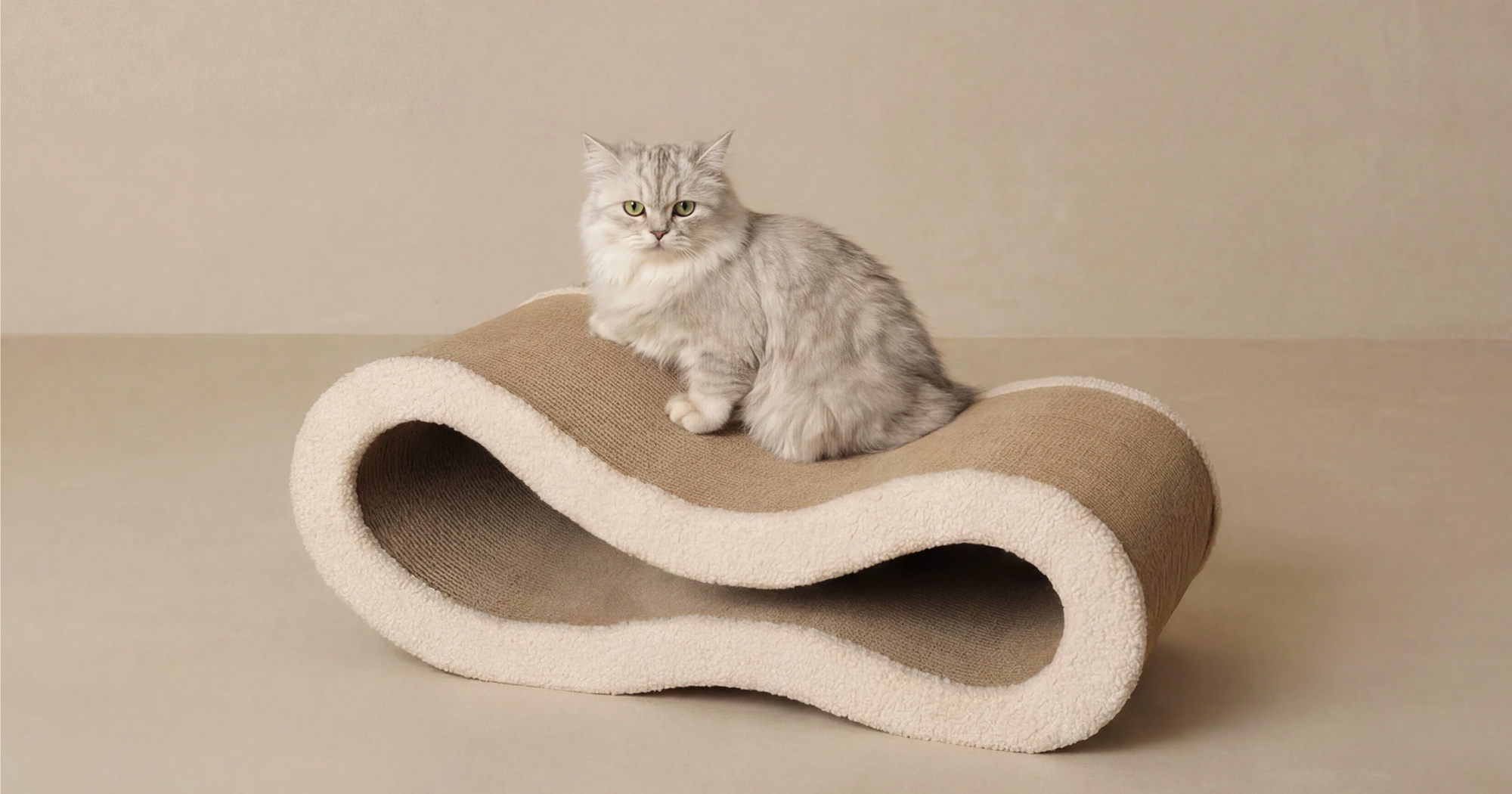 A luxury modern pet furniture piece, the Pet Jojo Cloud Lounge cat scratcher features a sculptural wave design with plush beige fabric edges and durable cardboard, with a silver cat lounging on top, showcasing a soft, premium, and elegant aesthetic.